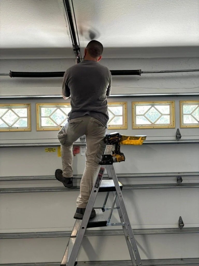 Technician on a ladder at the top of a white garage door