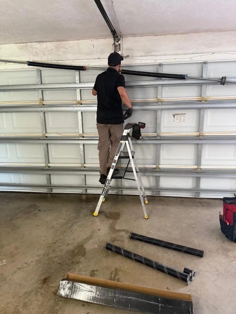 Technician on a ladder beside the opener rail with parts on the floor