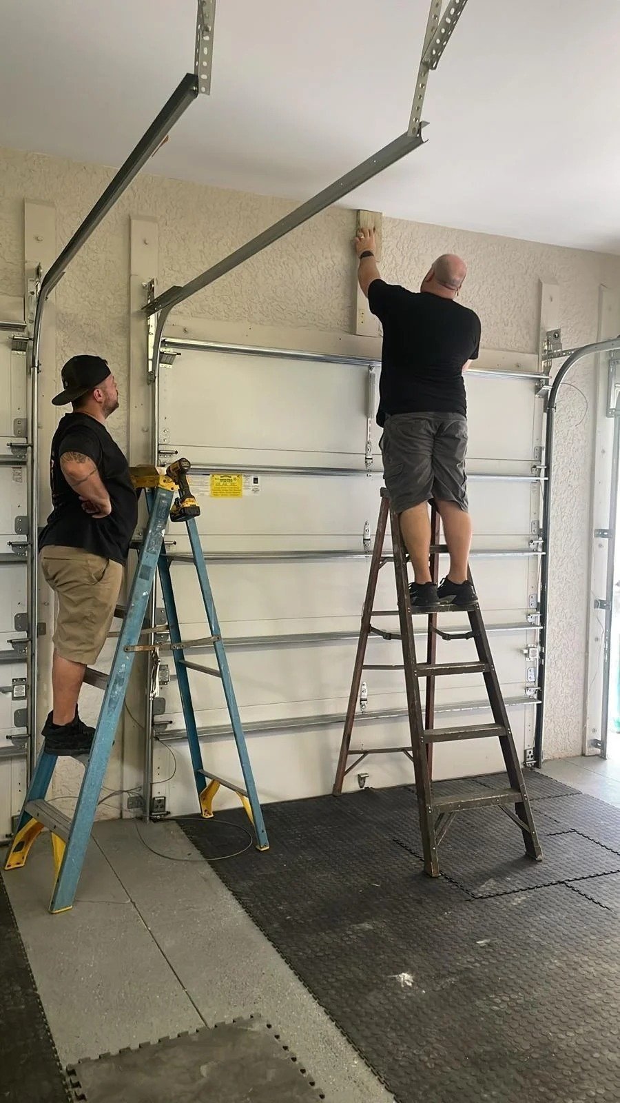 Technician on a tall ladder at the top rail of a garage door
