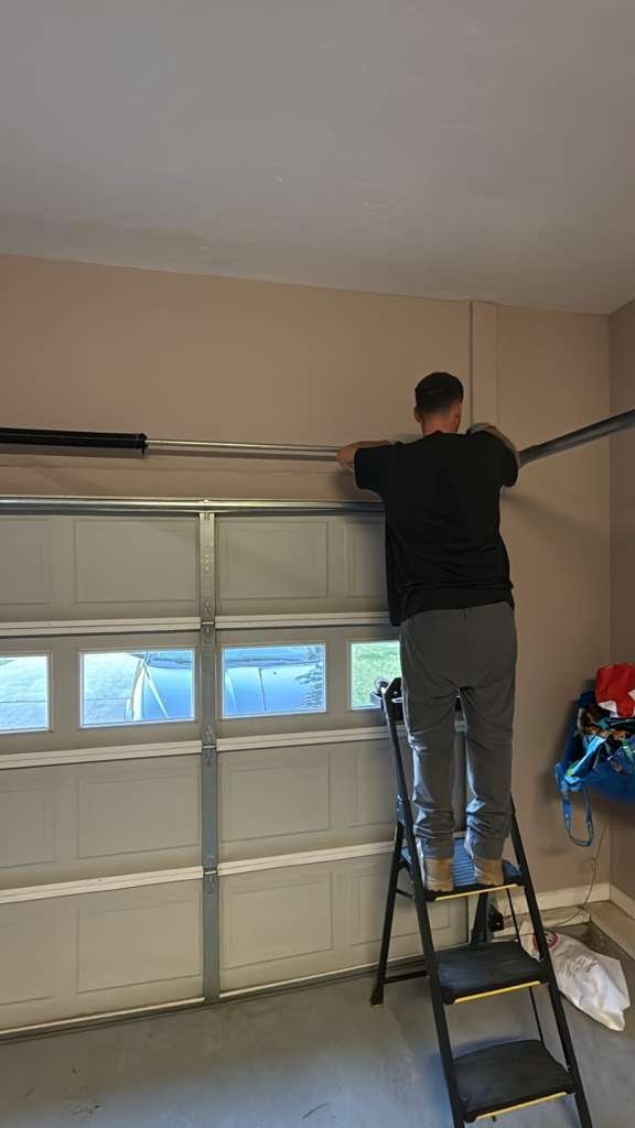 Technician on a ladder inside a garage with a windowed door