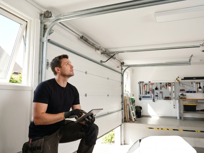 Technician kneeling beside a garage door with a tool in hand