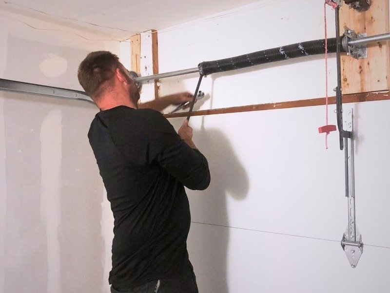 Technician reaching up to the torsion spring above a garage door